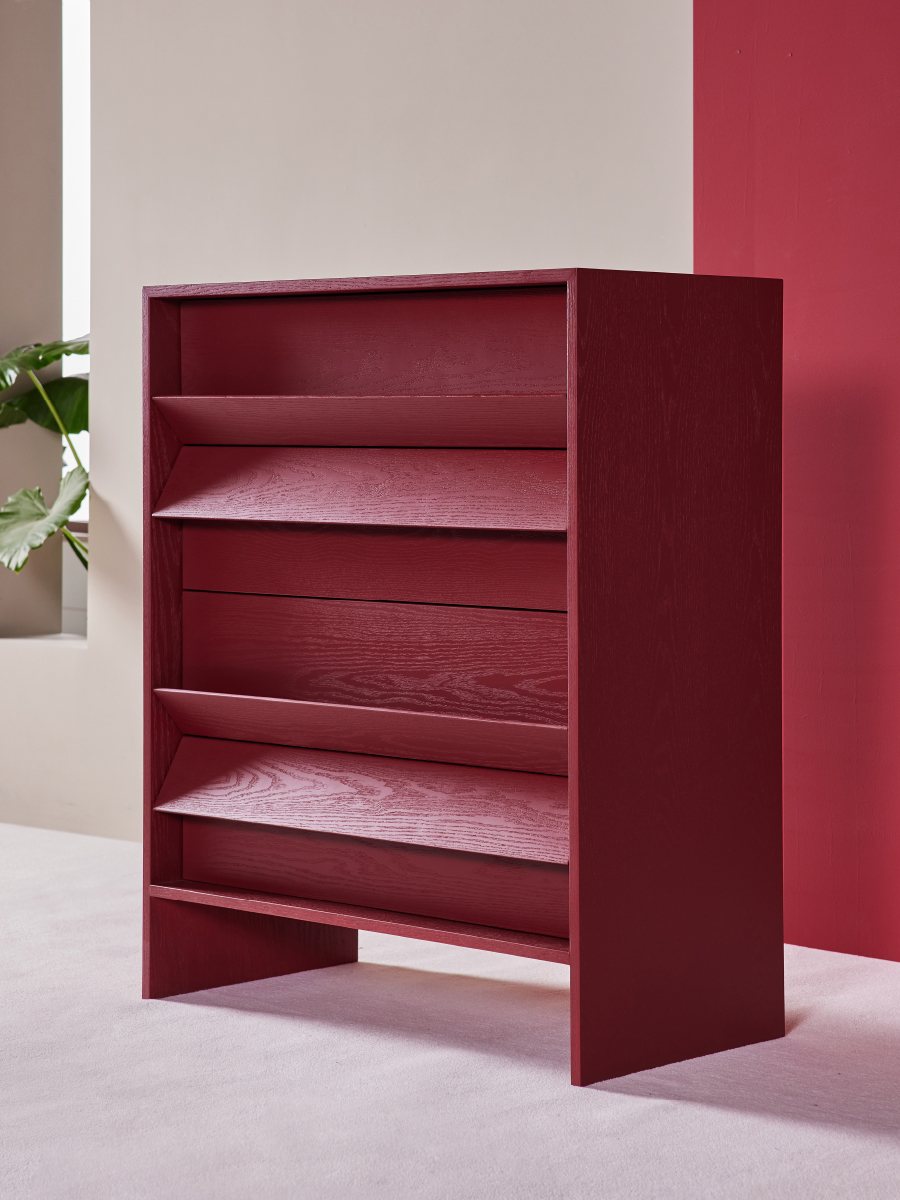 Tilt Chest in deep burgundy, three-quarter view showing the sloped and flat drawer fronts